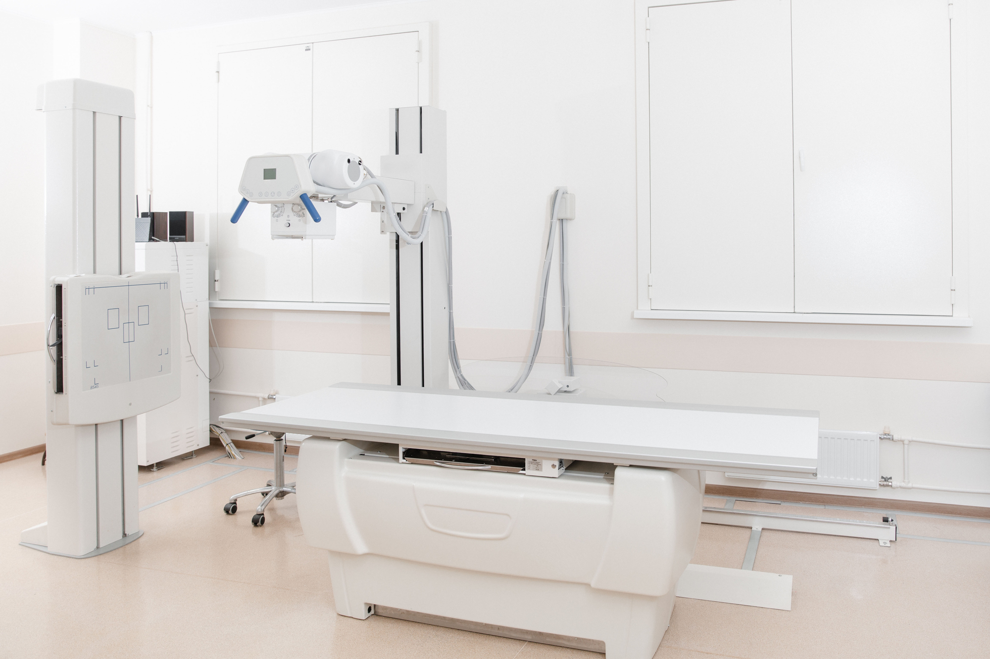 X-ray department in modern hospital. Radiology room with scan machine with empty bed. Technician adjusting an x-ray machine. Scanning chest, heart, lungs in modern clinic office