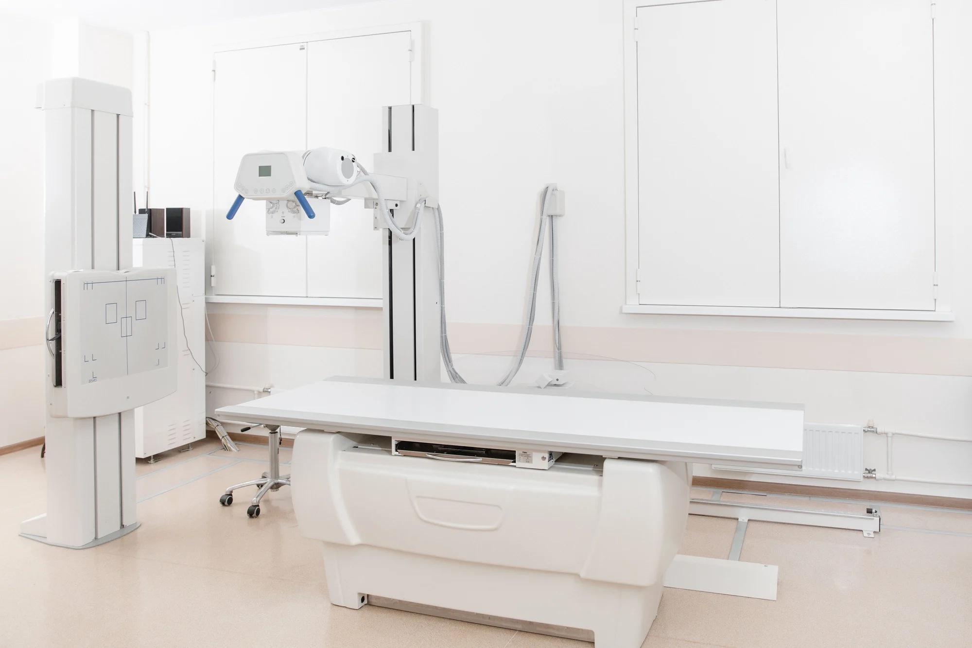 X-ray department in modern hospital. Radiology room with scan machine with empty bed. Technician adjusting an x-ray machine. Scanning chest, heart, lungs in modern clinic office X-ray department in modern hospital. Radiology room with scan machine with empty bed. Technician adjusting an x-ray machine. Scanning chest, heart, lungs in modern clinic office