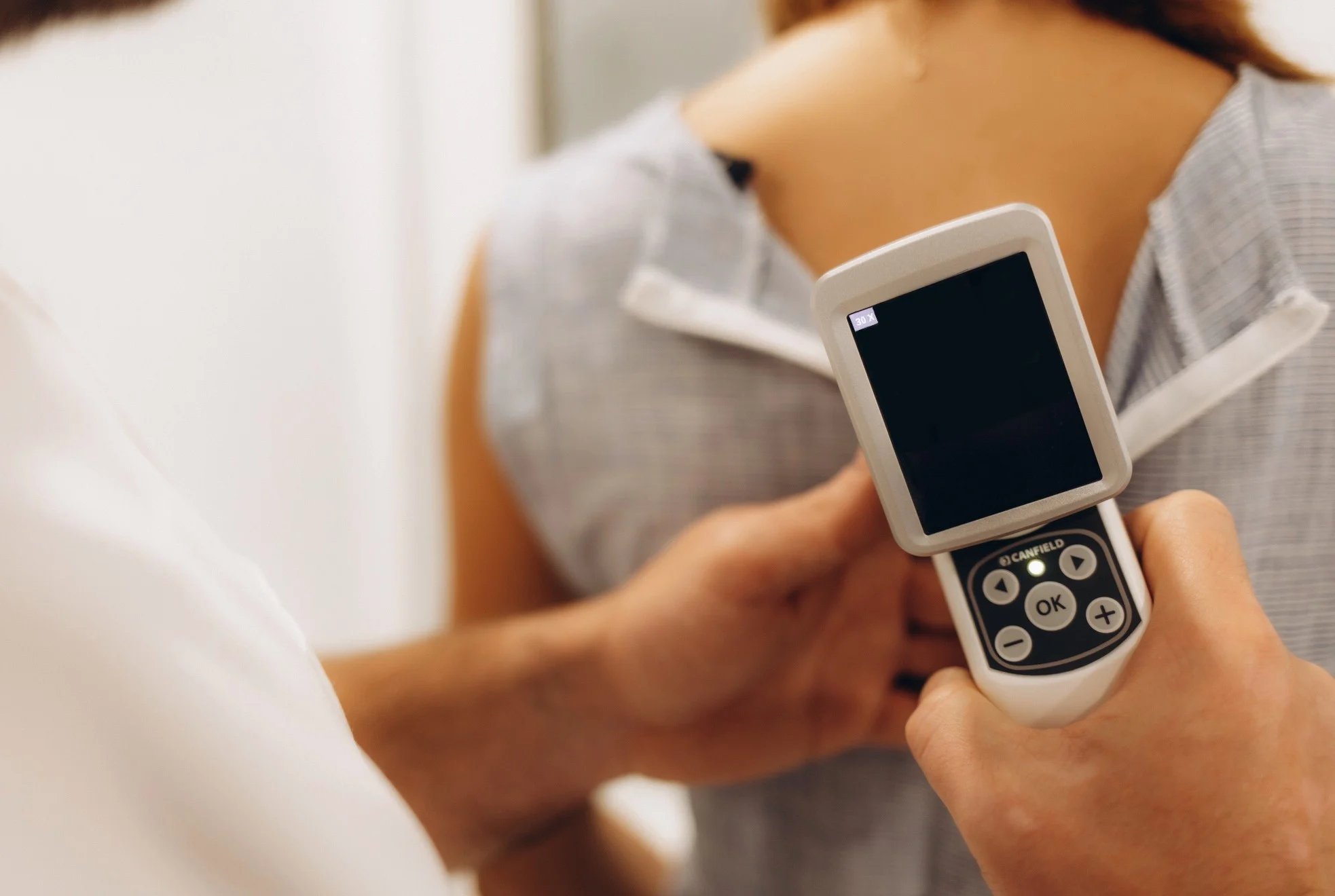 Depositphotos_743787788_L(1) Ärztin und Klientin in der Klinik für Dermatologie. Makrofoto des Dermatologen verwendet Dermatoskop für Gesichtshaut-Untersuchung.
