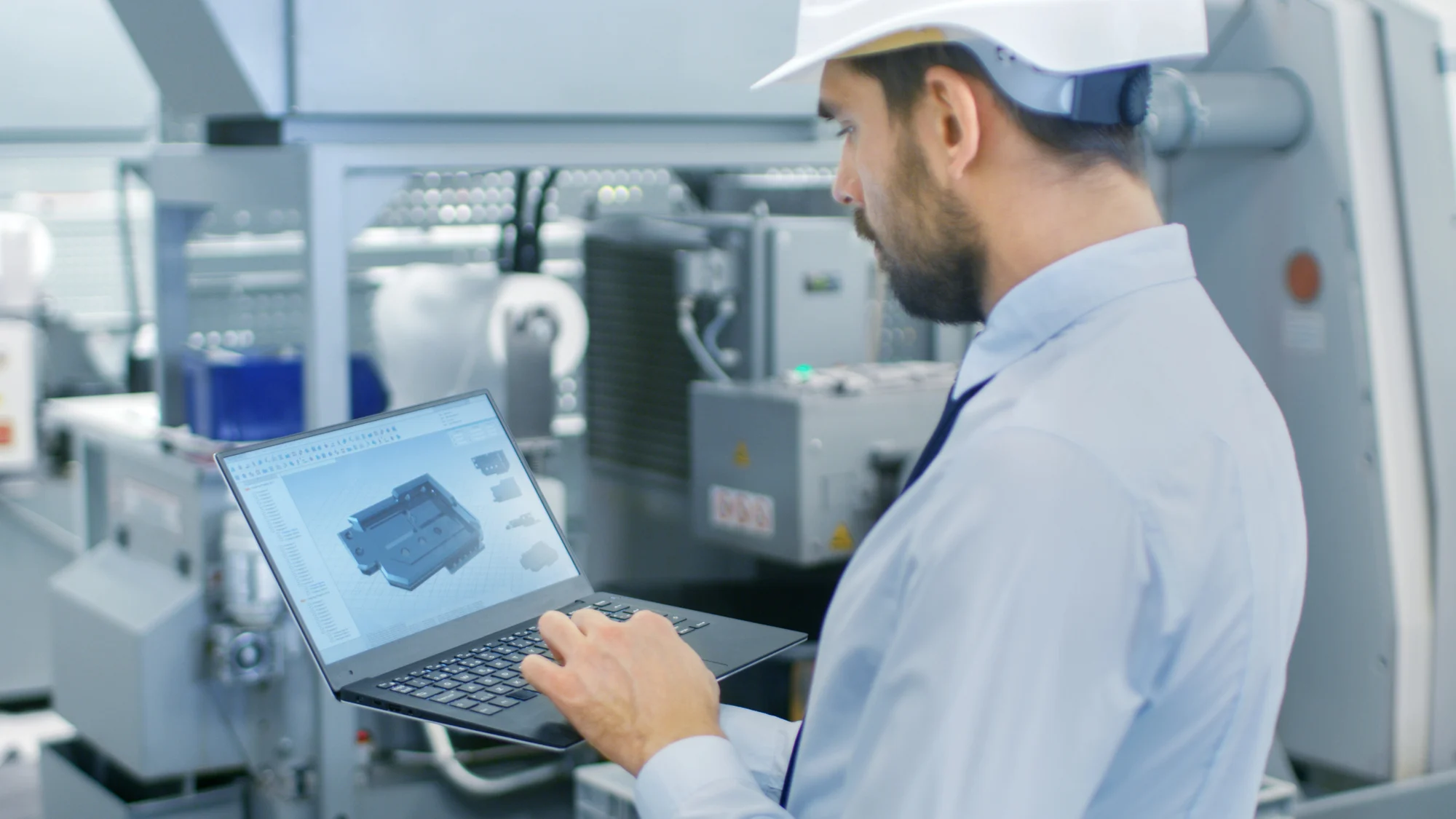 Depositphotos_222478980_L Der Chefingenieur im Bollenhut hält Laptop mit 3D-Modell auf dem Bildschirm. Im Hintergrund moderne Werksanlagen.